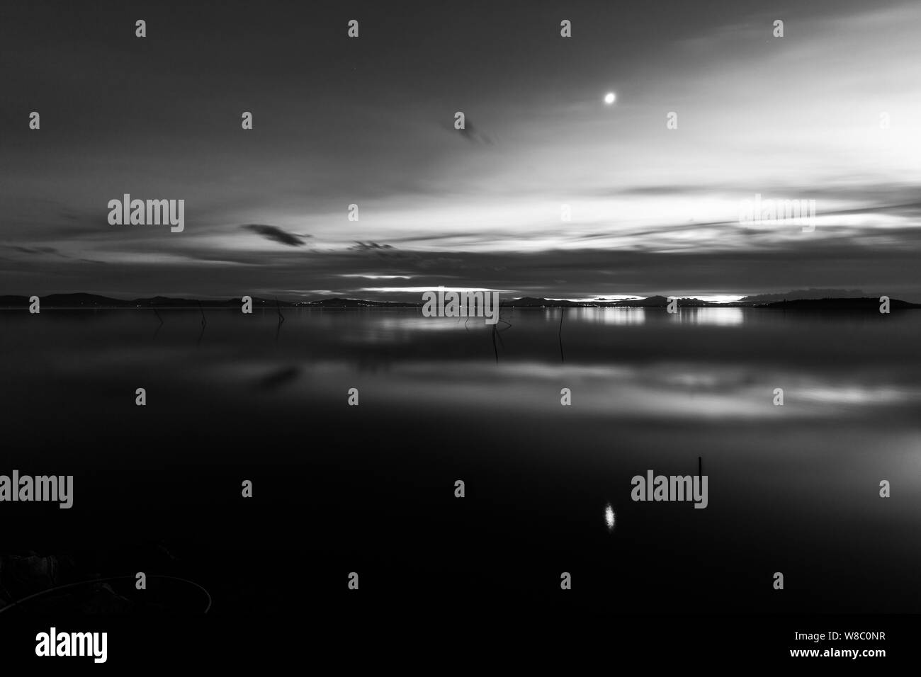 Luna por encima de un lago, con su reflexión sobre la superficie del lago Trasimeno al atardecer Foto de stock