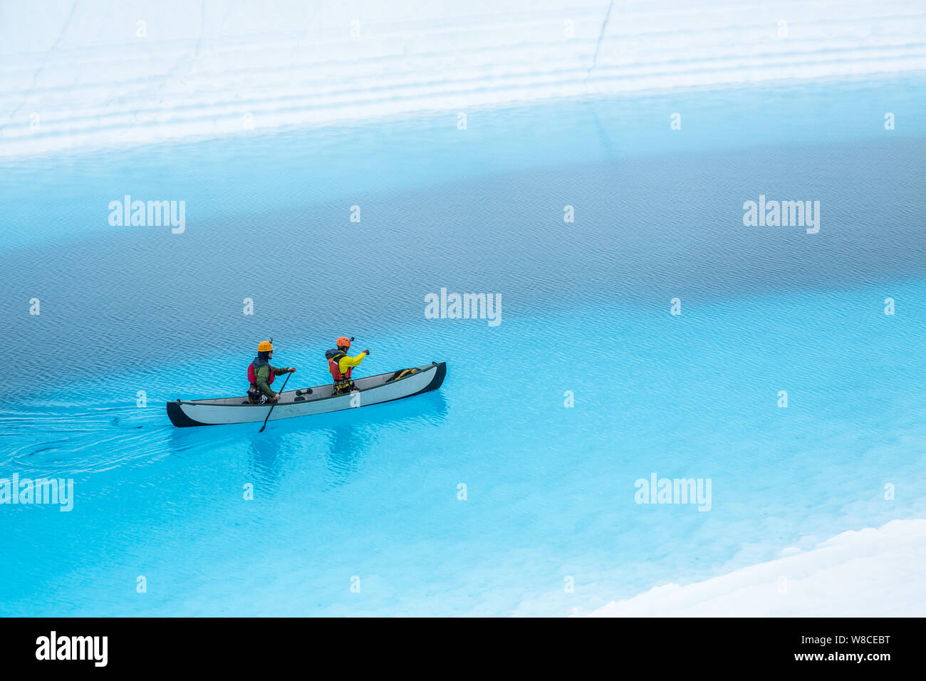 Dos hombres remar una canoa inflable en la parte superior de una piscina azul en el Glaciar Matanuska en el desierto de Alaska. El lago azul es un lago supraglacial, Foto de stock