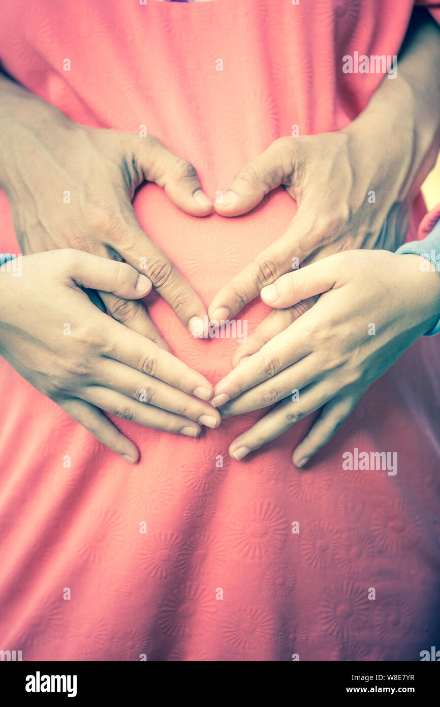 La mujer embarazada y su marido, sosteniendo sus manos en forma de corazón sobre su baby bump. Foto de stock