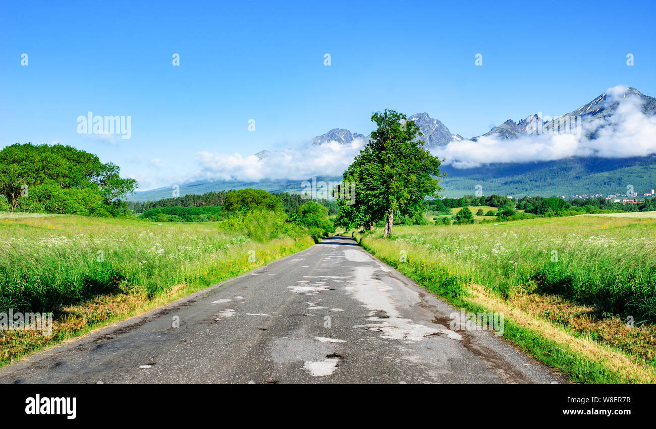 Carretera de asfalto entre los campos con el telón de fondo de un paisaje de montaña. Foto de stock