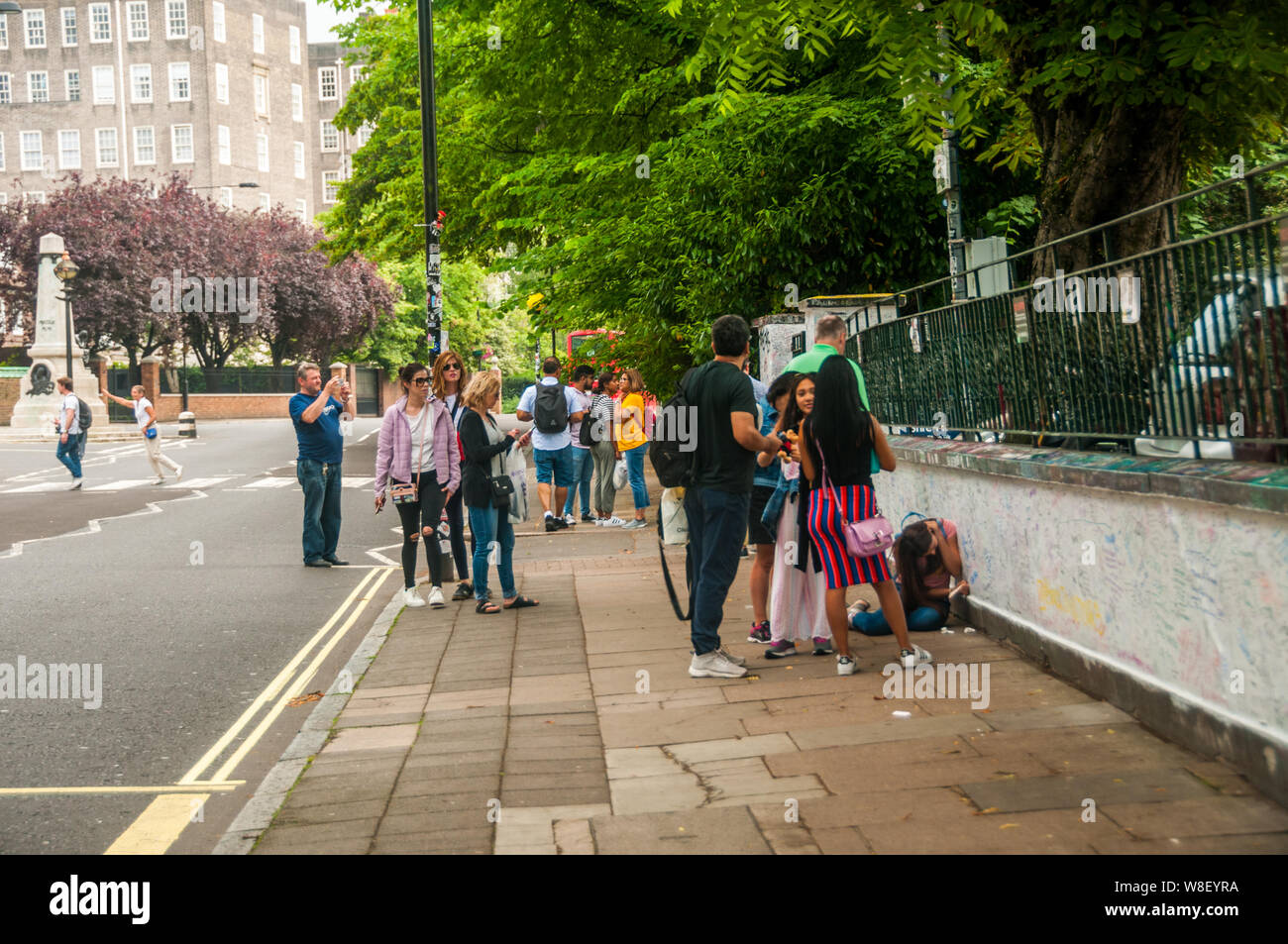 Los turistas con el graffiti en las paredes fuera de los estudios Abbey Road de Londres con el famoso cruce por detrás. Foto de stock