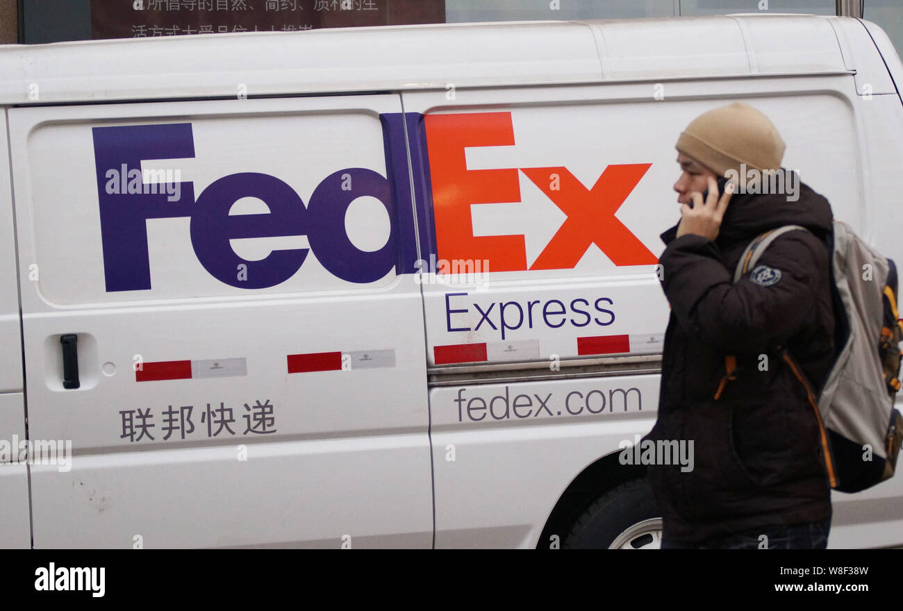 --FILE--un peatón hablando por su teléfono móvil camina pasado un vehículo de entrega de FedEx Express en una carretera en Tianjin, China, 22 de enero de 2013. FedEx Corp está Foto de stock