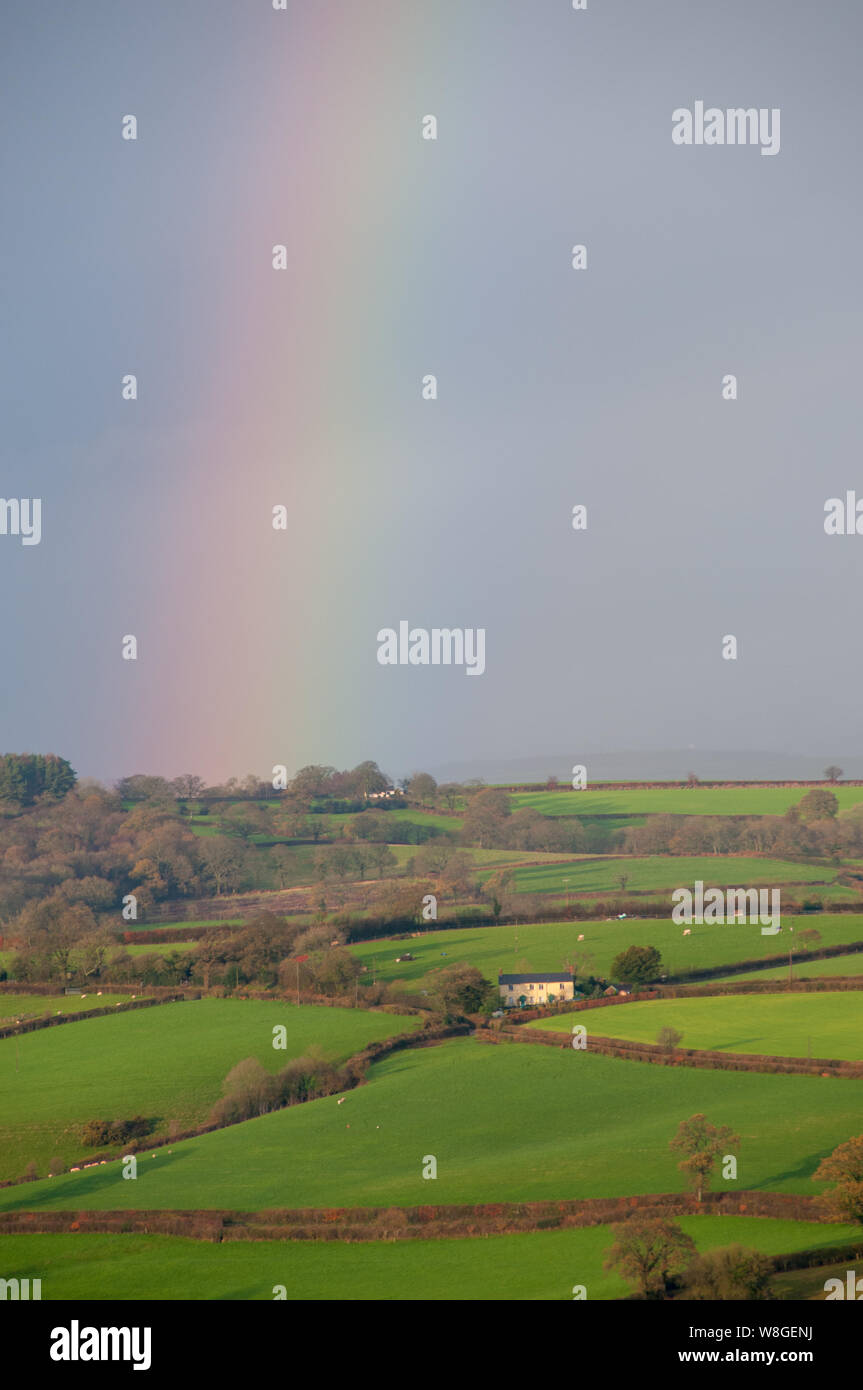 El campo se ilumina en esta hermosa mañana de Dewey en Warwick, Inglaterra. La lluvia dejó de caer y un arco iris llena el cielo como los rayos del sol hacia abajo. Foto de stock