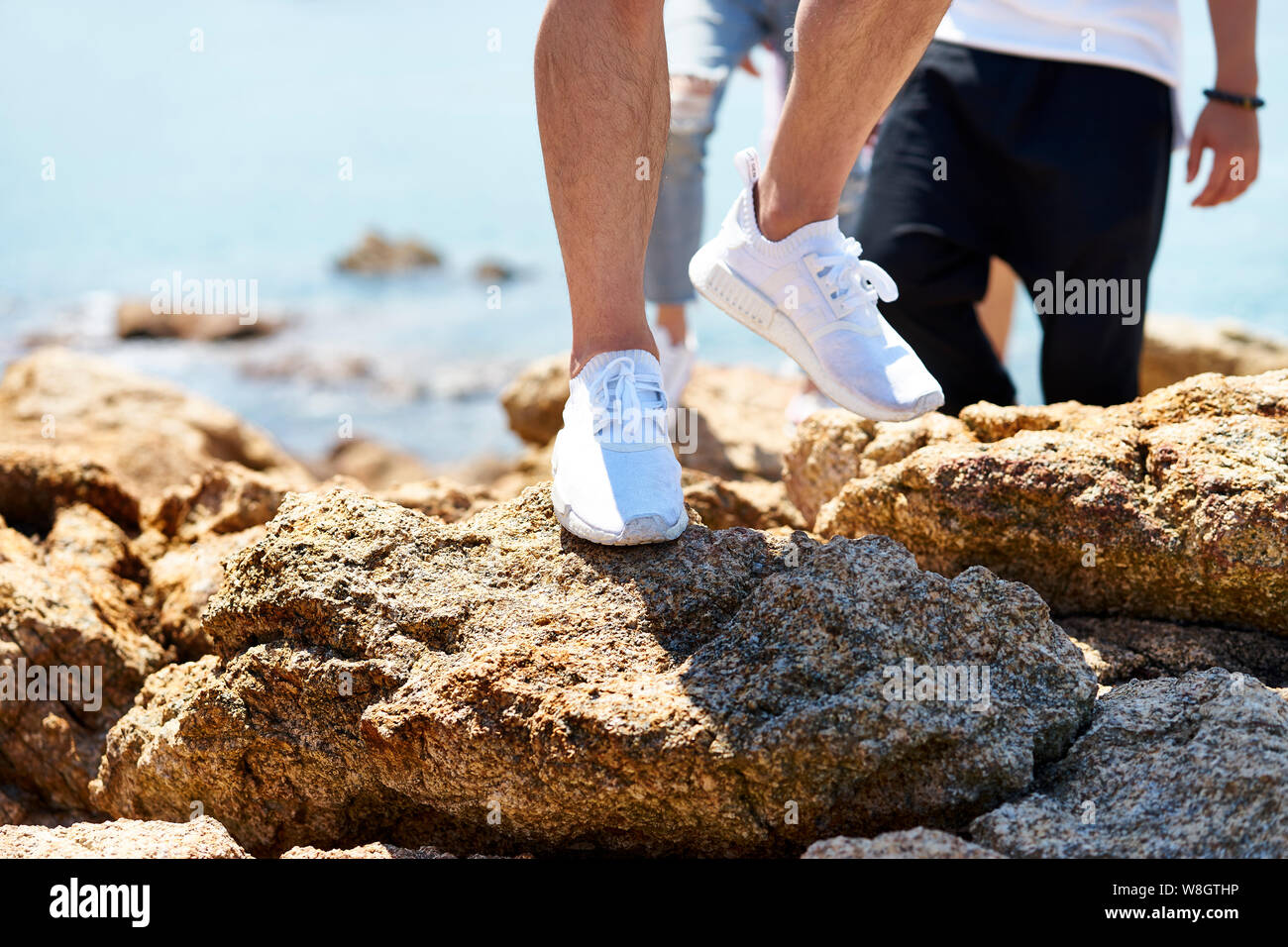Primer plano de los pies de la joven caminando sobre las rocas por el mar Foto de stock
