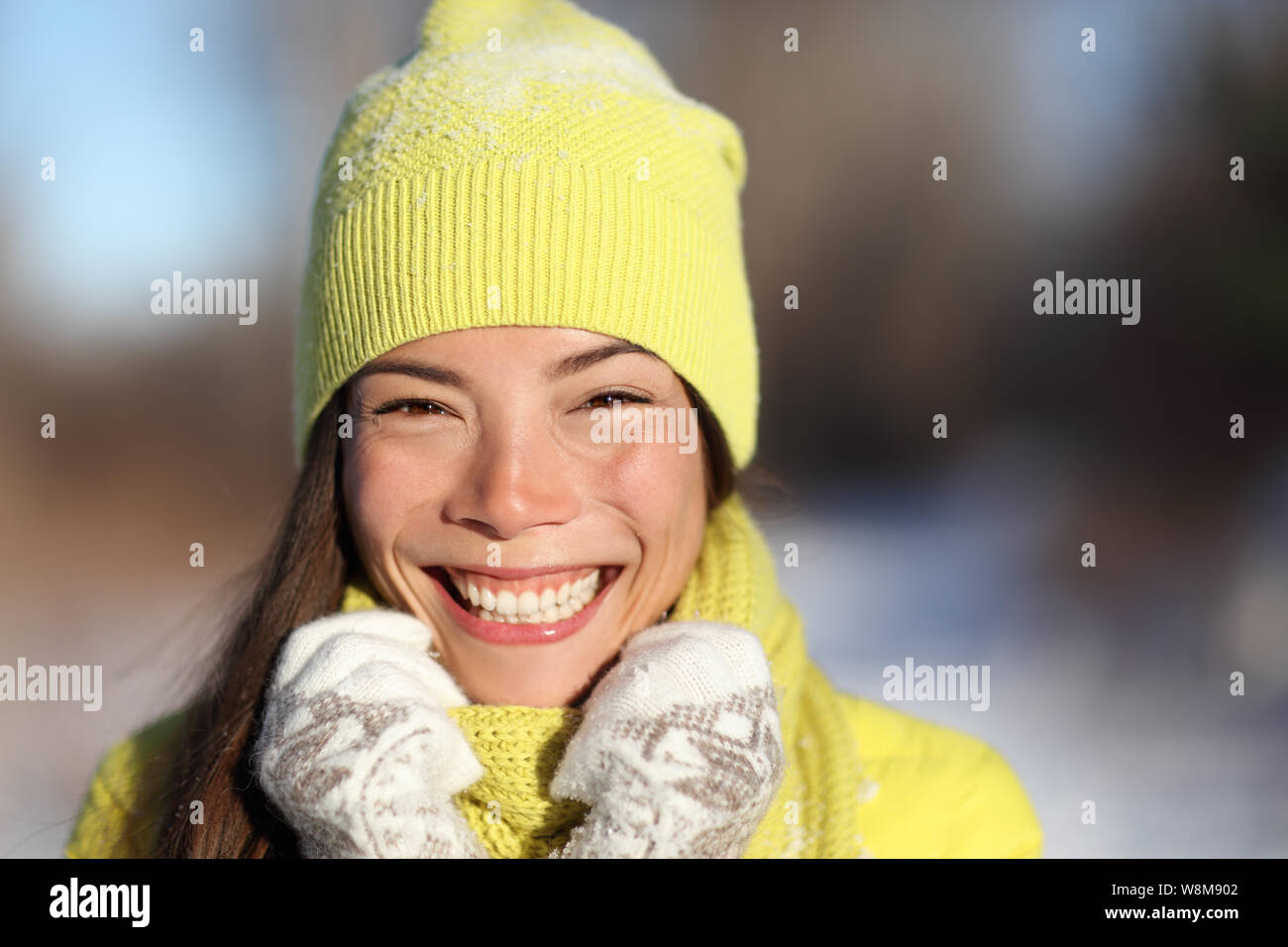Temporada de invierno chica sonriente divirtiéndose afuera en la nieve. Retrato de mujer asiática feliz lúdico al aire libre con sonrisa saludable en los soleados días de invierno vistiendo ropa amarilla gorra gorro y guantes. Foto de stock