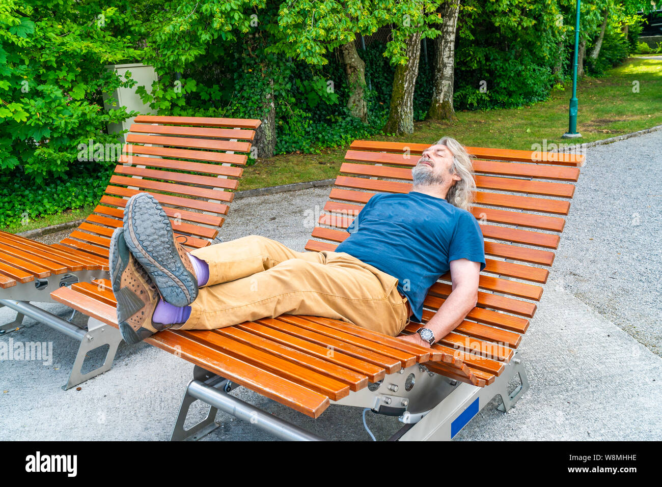 Un varón de mediana edad relajándose en una silla mecedora de madera en el parque público. Foto de stock
