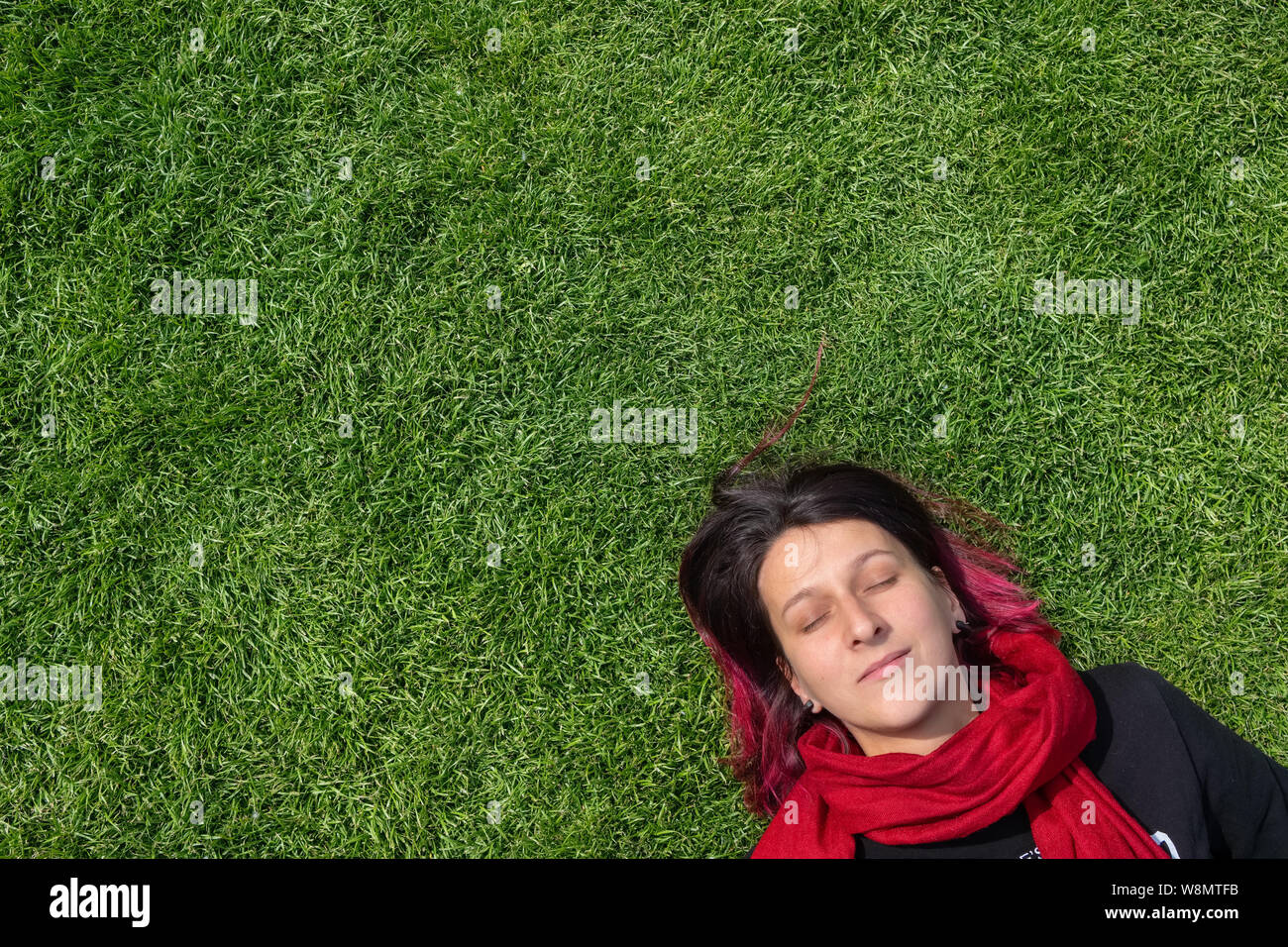 Retrato de una joven mujer soñando sobre un césped verde con los ojos cerrados Foto de stock