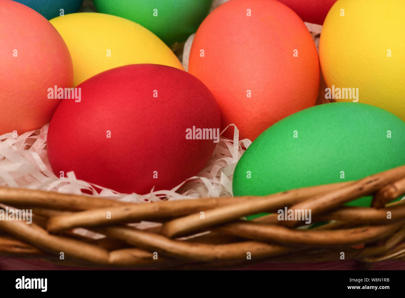 Grandes huevos de Pascua de colores diferentes que se encuentran en una cesta de mimbre. Fotografía horizontal Foto de stock