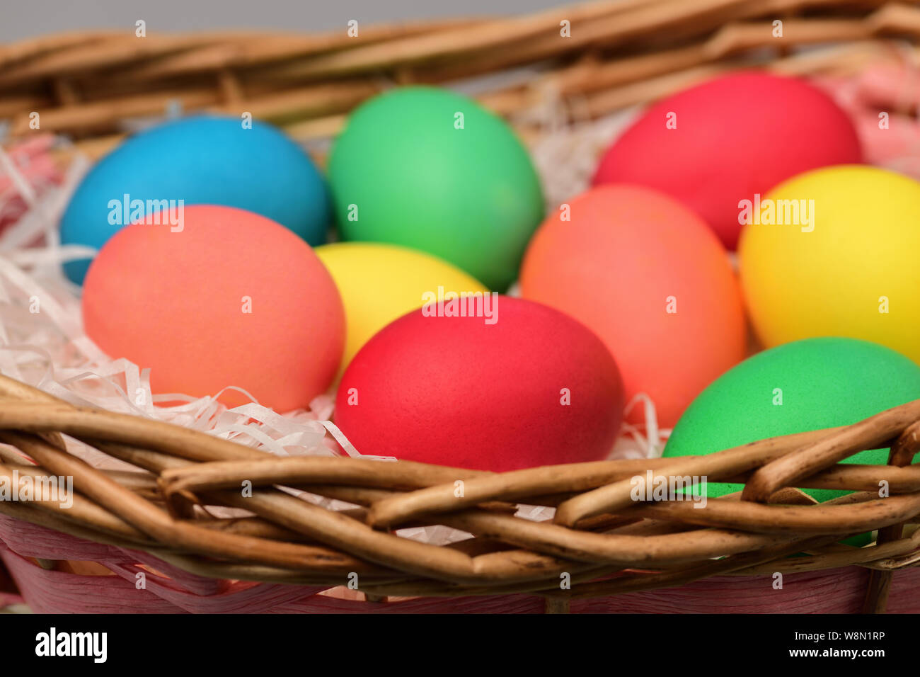 Huevos de Pascua de colores diferentes que se encuentran en una cesta de mimbre cerca. Fotografía horizontal Foto de stock