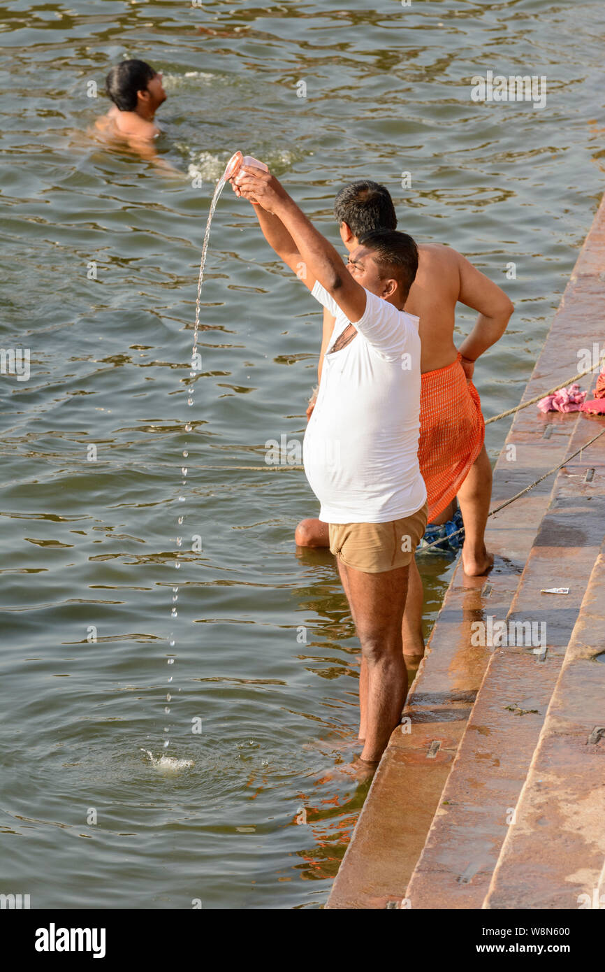 Un Hindú hombre vierte las ofrendas a los dioses (libaciones) en el río Ganges en Varanasi, Uttar Pradesh, India, el sur de Asia. Foto de stock