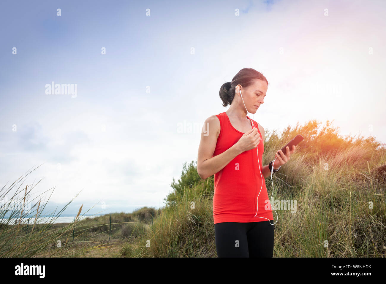 Mujer con auriculares, auriculares, controlar su teléfono móvil después de hacer ejercicio en el exterior Foto de stock