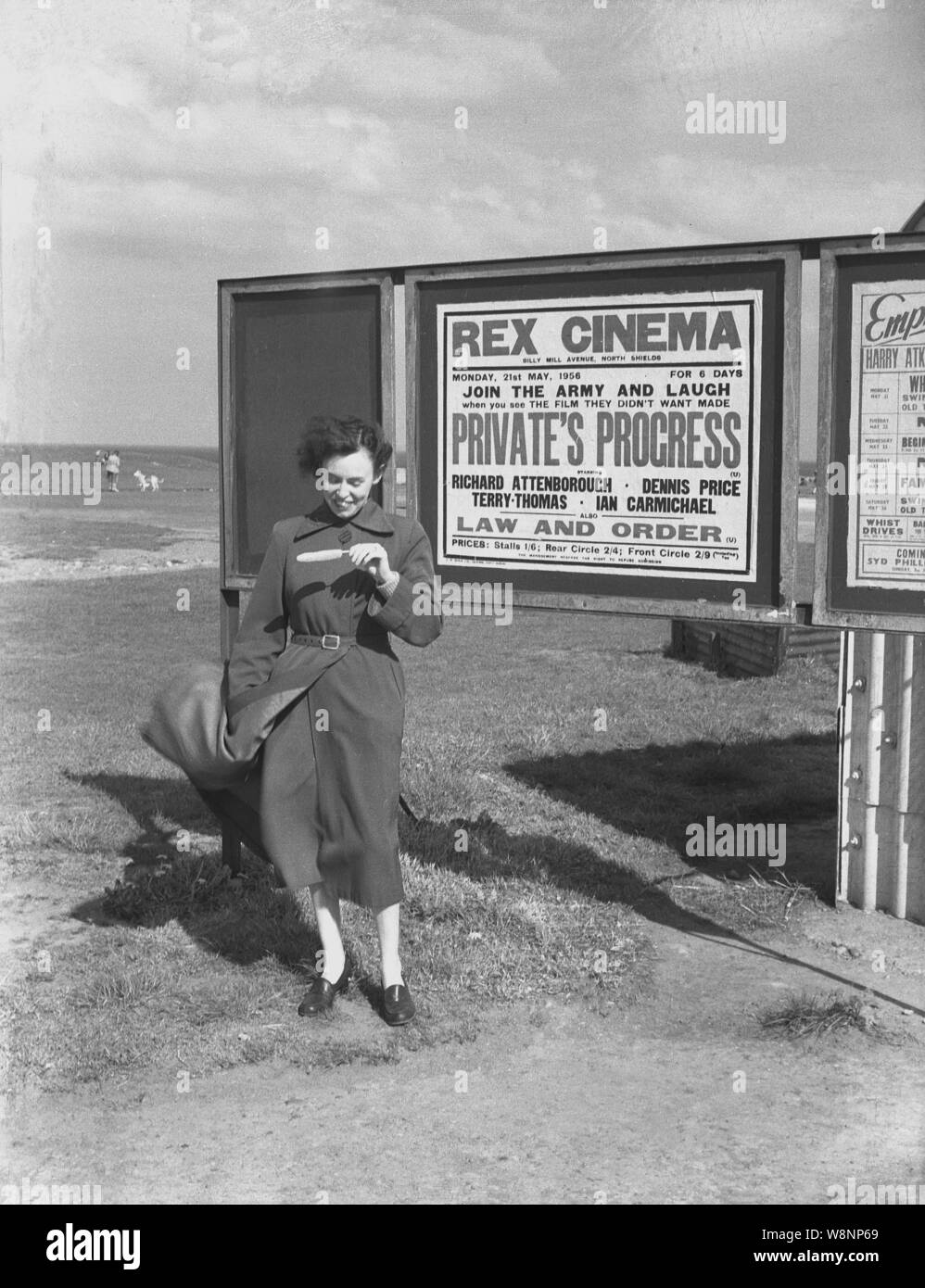 1956, histórico, una dama con una máquina de paleta de helado de pie fuera un tablero de aviso