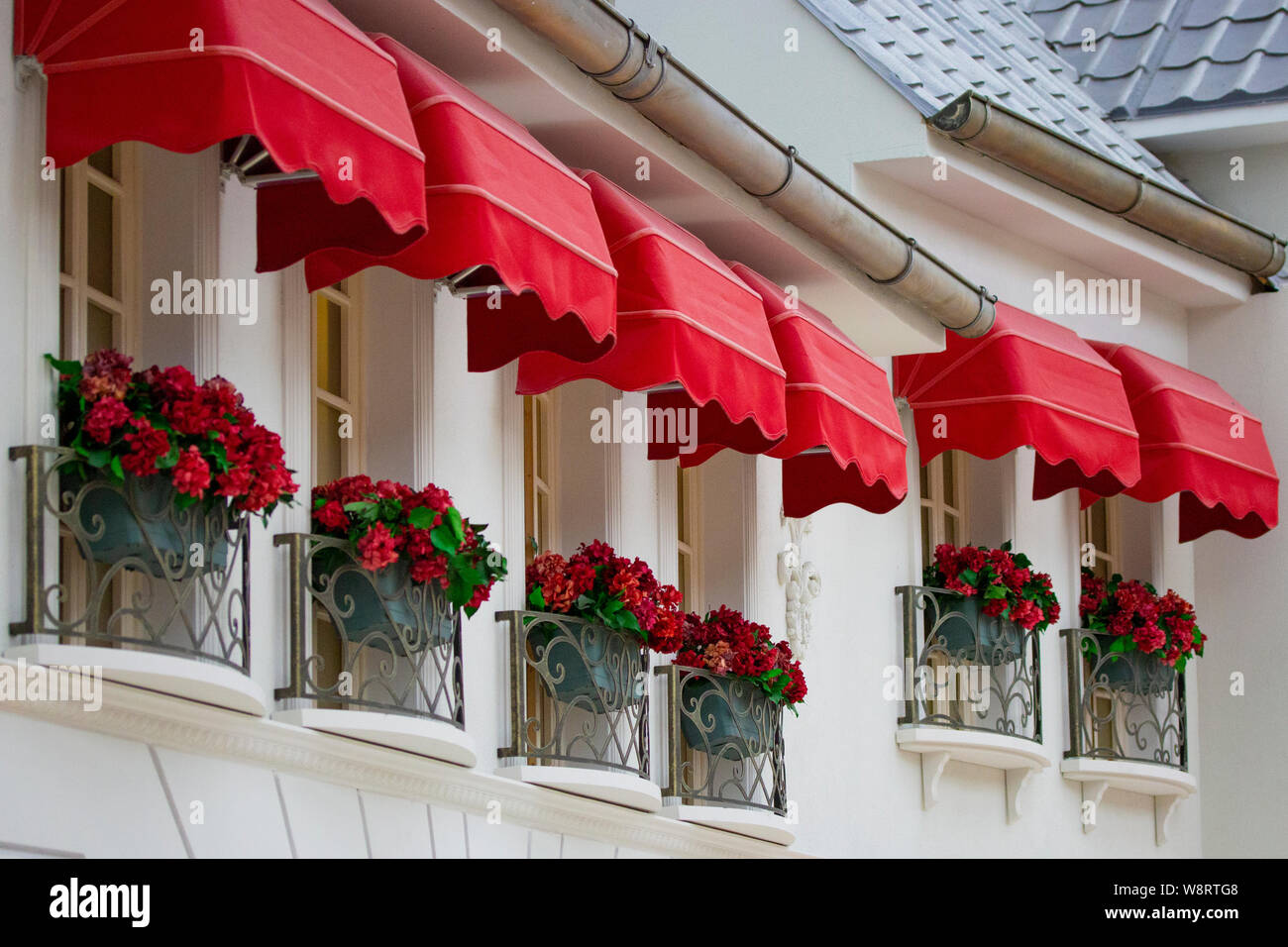 Hermosas ventanas altas con flores rojas y un balcón de hierro forjado alero  marquesina roja sobre una pared blanca Fotografía de stock - Alamy