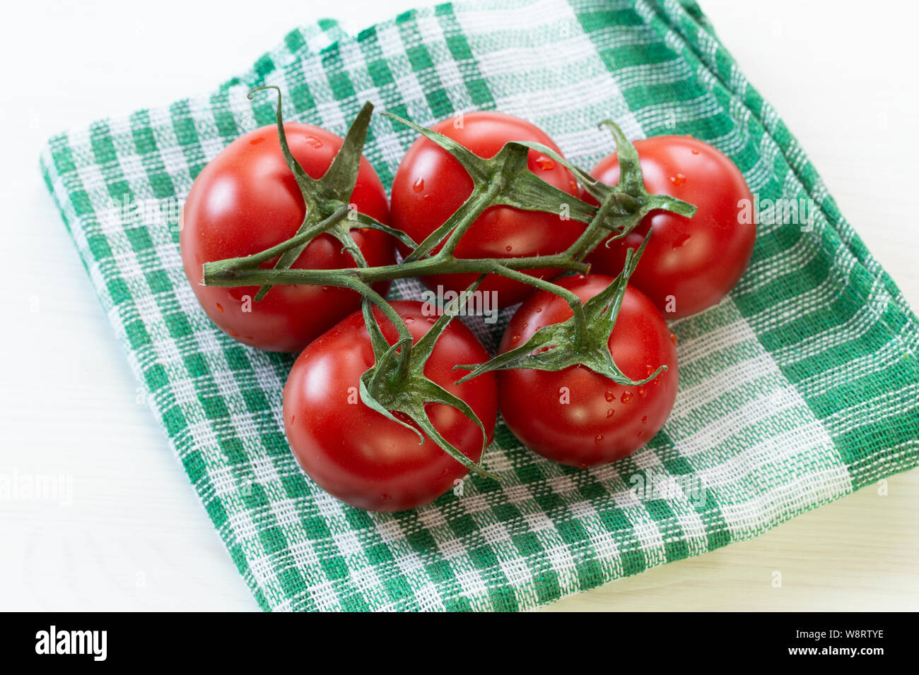 Una rama de deliciosos tomates orgánicos frescos rojas maduras en una  servilleta a cuadros verde. Ronda hermoso tomates medianos con hojas en una  rama Fotografía de stock - Alamy