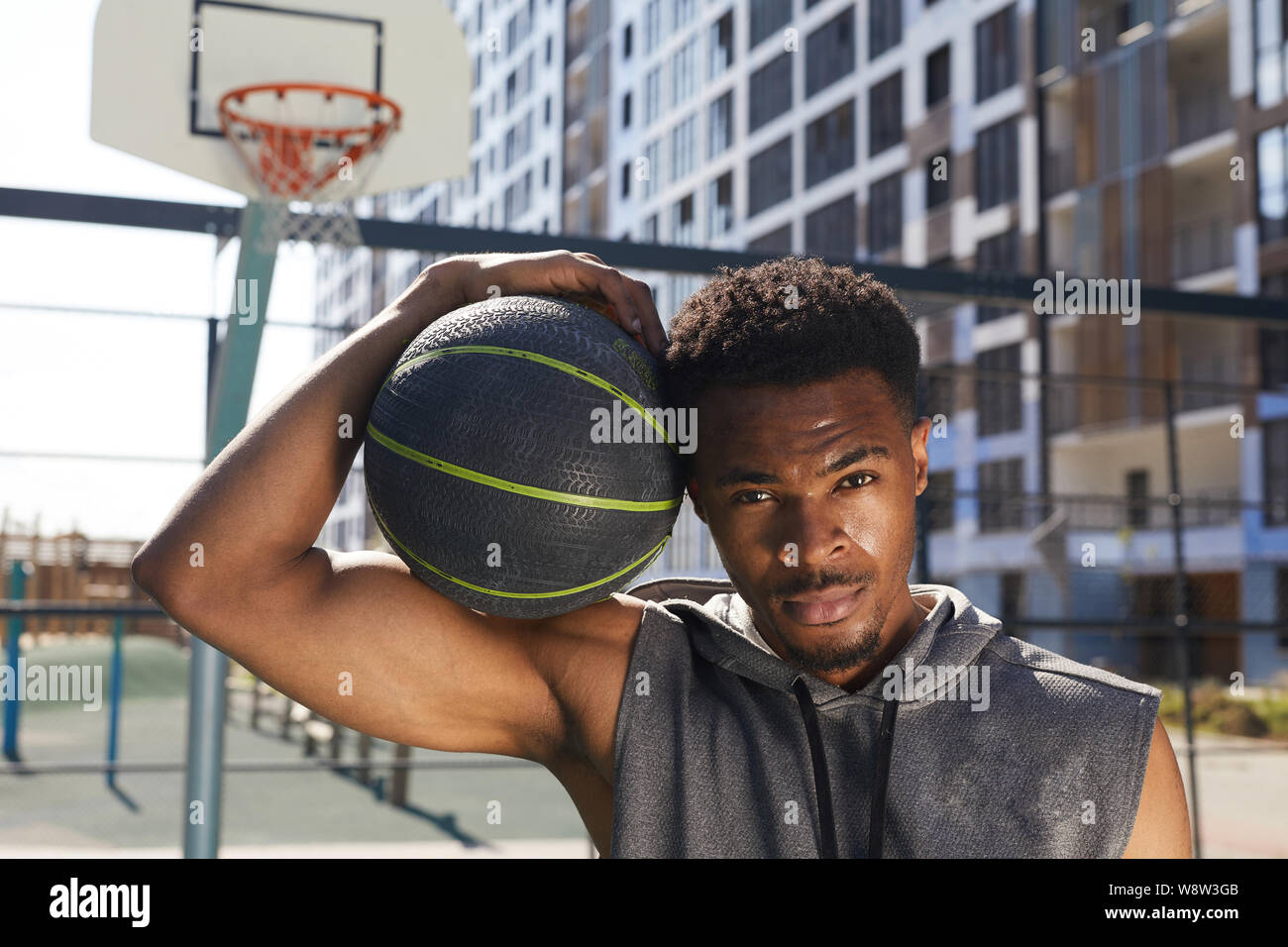 Retrato de apuesto hombre afroamericano la celebración de pelota de baloncesto mirando a la cámara mientras posan en la cancha de deportes al aire libre, espacio de copia Foto de stock
