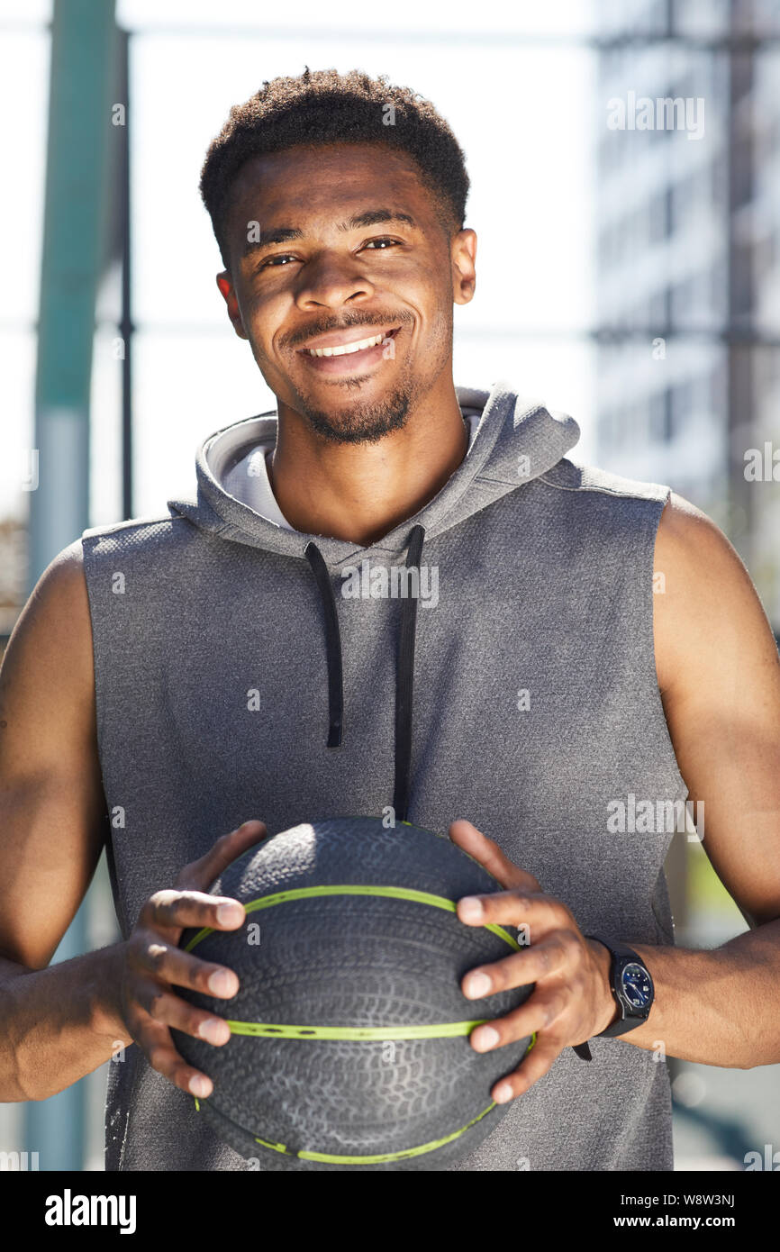 Cintura para arriba retrato del hombre africano muscular sosteniendo pelota de baloncesto al aire libre y sonriendo a la cámara , espacio de copia Foto de stock