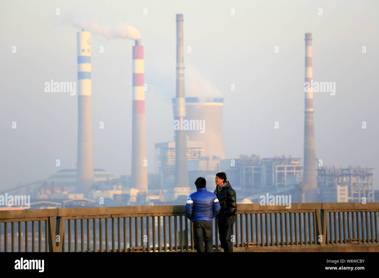--FILE--Dos hombres a hablar sobre un puente cerca de una central eléctrica de carbón en la ciudad de Jiujiang, provincia de Jiangxi de China oriental, el 23 de enero de 2014. Un proyecto revisado de Foto de stock