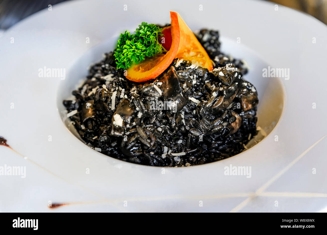 Un risotto negro con tinta de calamar rabas espolvoreado con queso  parmesano, servidos con una rodaja de naranja y perejil en un restaurante  de alta gama en Montenegro Fotografía de stock -