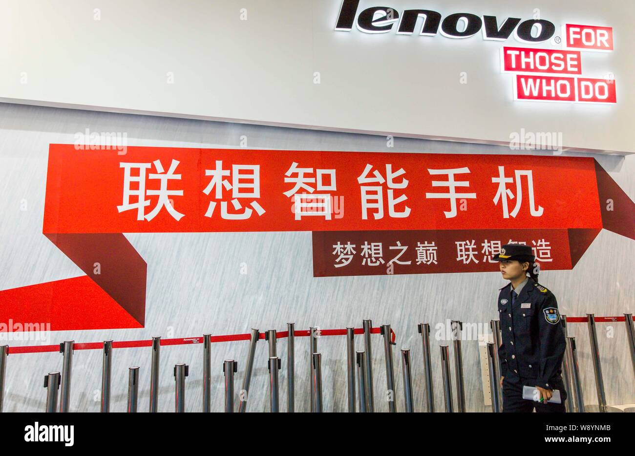--FILE--Una mujer guardia de seguridad camina pasado un anuncio de Lenovo durante el PT/EXPO COMM China 2013, en Beijing, China, 24 de septiembre de 2013. Micr Foto de stock