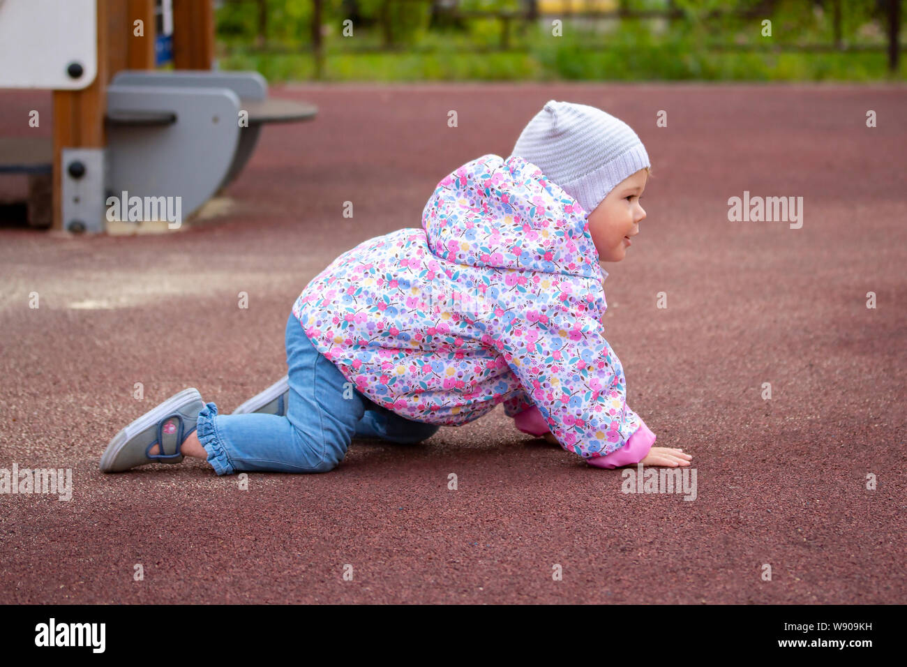 Baby Girl arrastrándose a cuatro patas en el patio de recreo. Un niño en caliente pantalones vaqueros ropa hat jacket 1 año de edad el bebé camina cerca de la casa