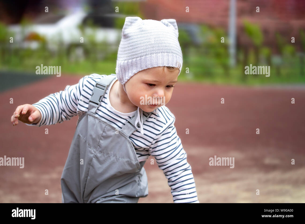 Bebé niña niño de 1 año de edad gris, Sombrero y pantalones con tirantes, una caminata. de un niño de 1 año en el patio de recreo Fotografía de