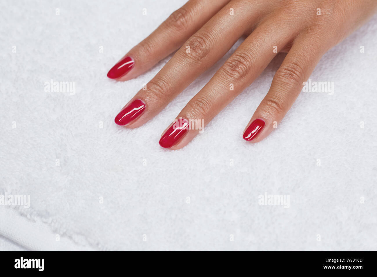 Esmalte de uñas de color rojo mujer manicura, tratamiento de spa en mano toalla blanca Foto de stock