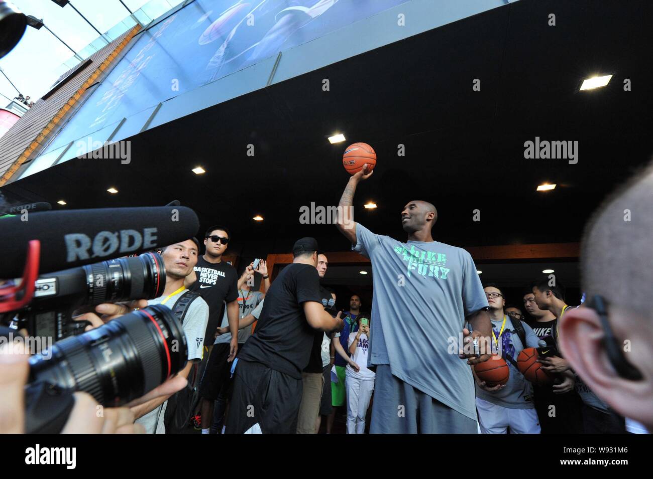 La estrella de la NBA Kobe Bryant, centro, se prepara para lanzar una  pelota de baloncesto a una multitud de fans durante un evento promocional  en una tienda de ropa deportiva de