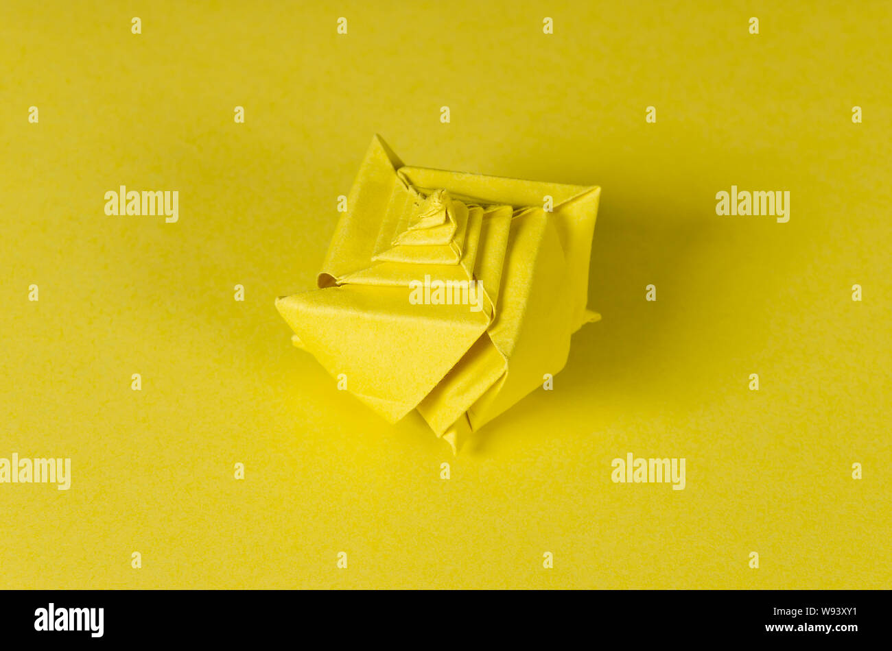 Concha de origami de color amarillo sobre fondo amarillo. Arte japonés de plegado de papel. Hoja de papel cuadrado plano trasladados en una escultura terminada. Foto de stock