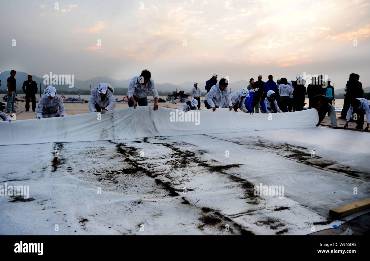 Los funcionarios enrollar un trozo de seda, en la que el artista contemporáneo chino Cai Guoqiang pintados de primavera con pólvora en una plataforma en el lago Oeste i Foto de stock