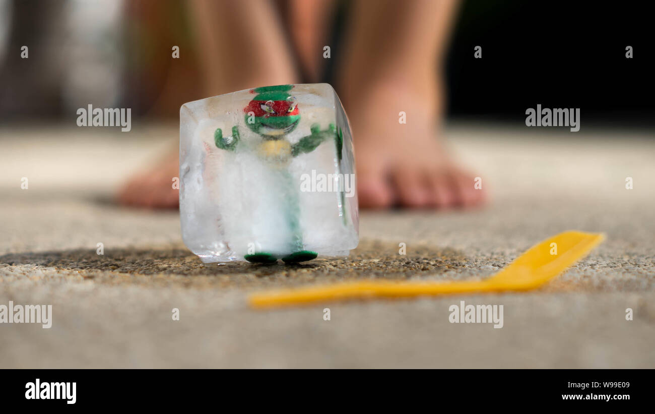 Tortugas Ninja atrapado en el cubo de hielo, la fusión en el sol enfrente de niños pies Foto de stock