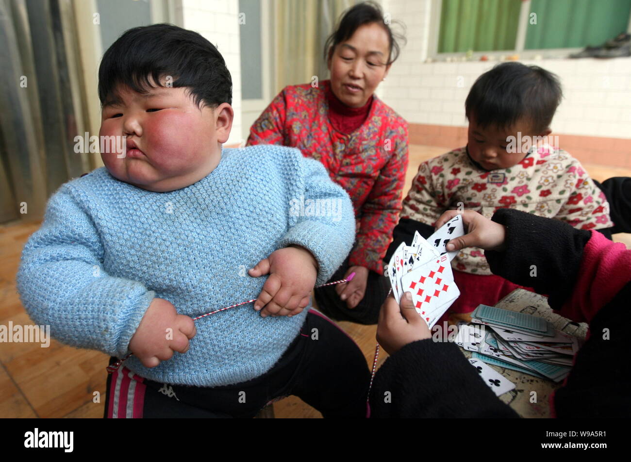 Pang Ya (izquierda), de 2 años de edad, juega al póquer con niños normales de la misma edad junto a su abuela en su casa en la ciudad, la ciudad de Yuncheng Taocun, Northwest Foto de stock