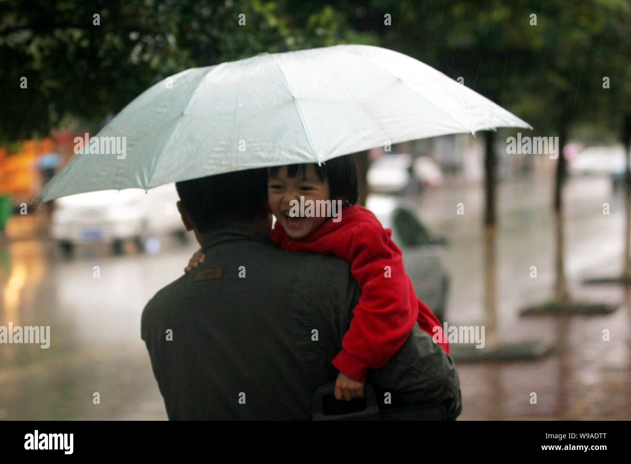 Un hombre chino mantiene un sonriente niño camina en la lluvia en Kunming, en el suroeste de la provincia de Yunnan, en China el 28 de marzo de 2010. La lluvia artificial humedecido pa Foto de stock