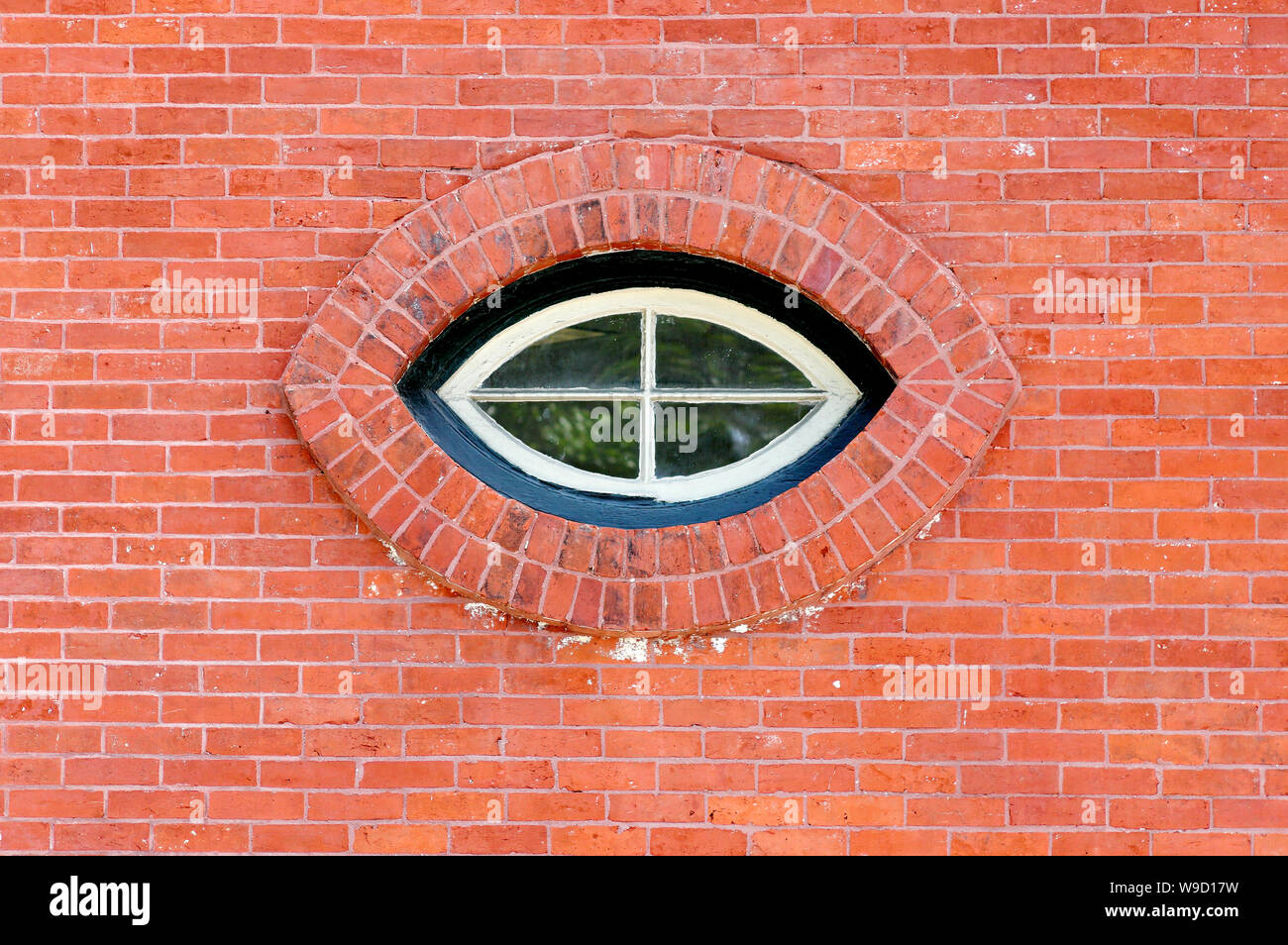 Ventana con forma de ojo de gato en una pared de ladrillo rojo Foto de stock