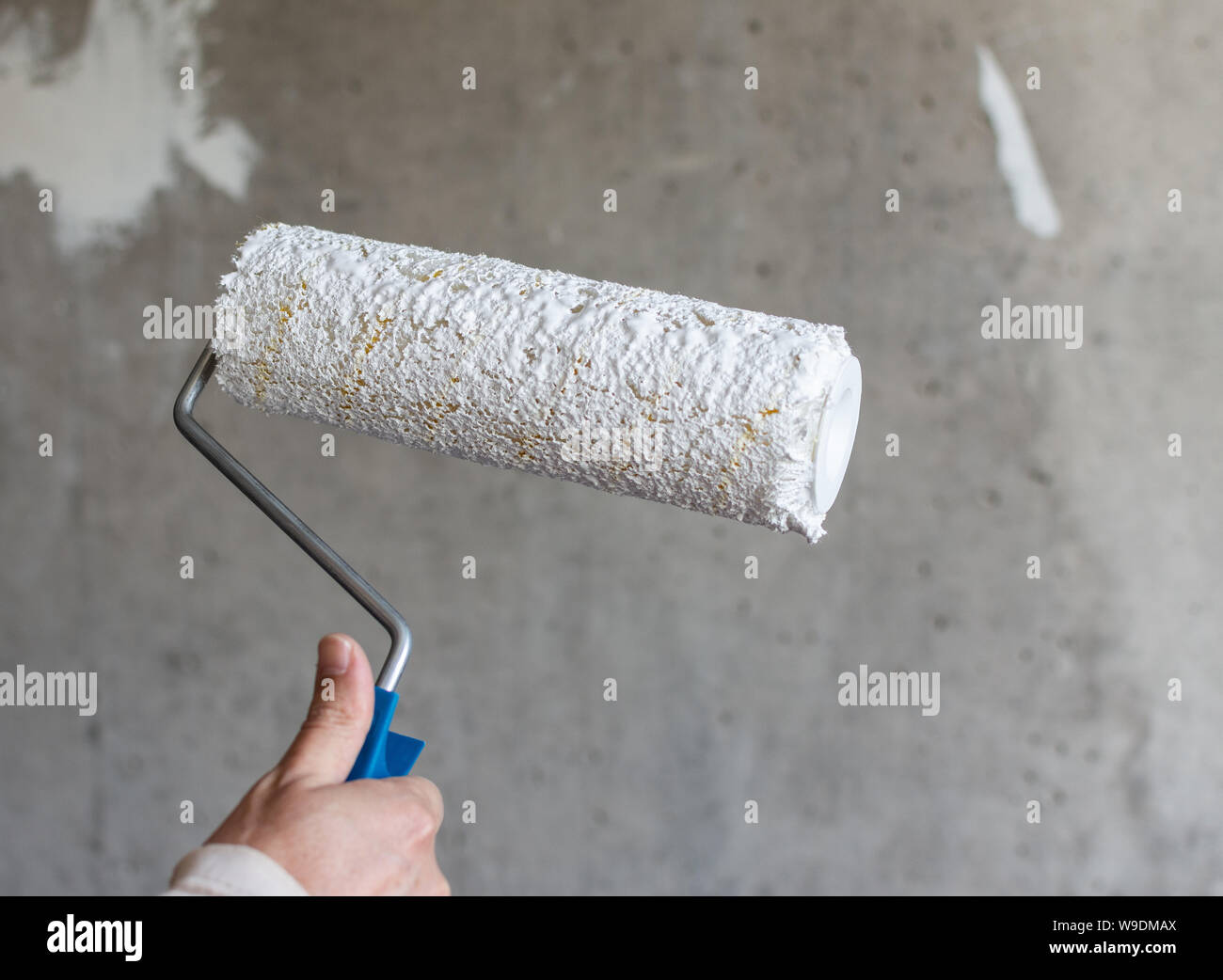 Un pintor pinta un muro de hormigón con pintura blanca, un macho de mano  con un rodillo de pintura para pintar una pared Fotografía de stock - Alamy