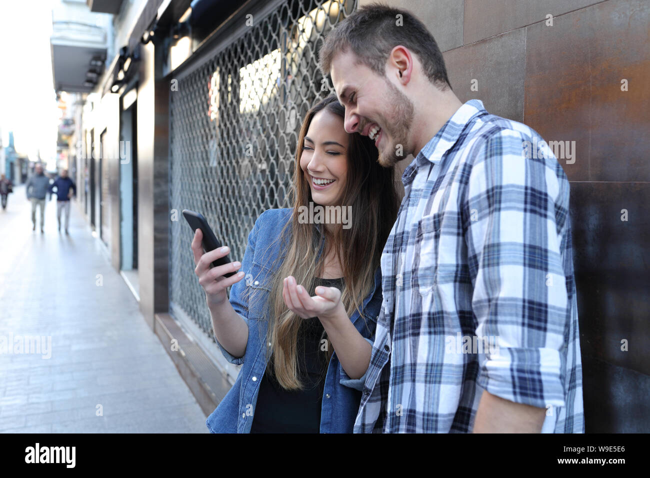 Feliz pareja sorprendente comprobar el contenido del teléfono inteligente de pie en la calle Foto de stock