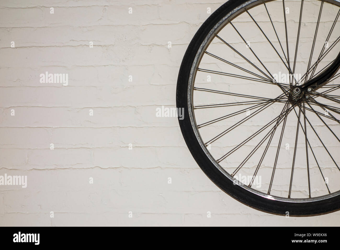 Rueda de bicicleta negro contra paredes de ladrillo blanco. Foto de stock