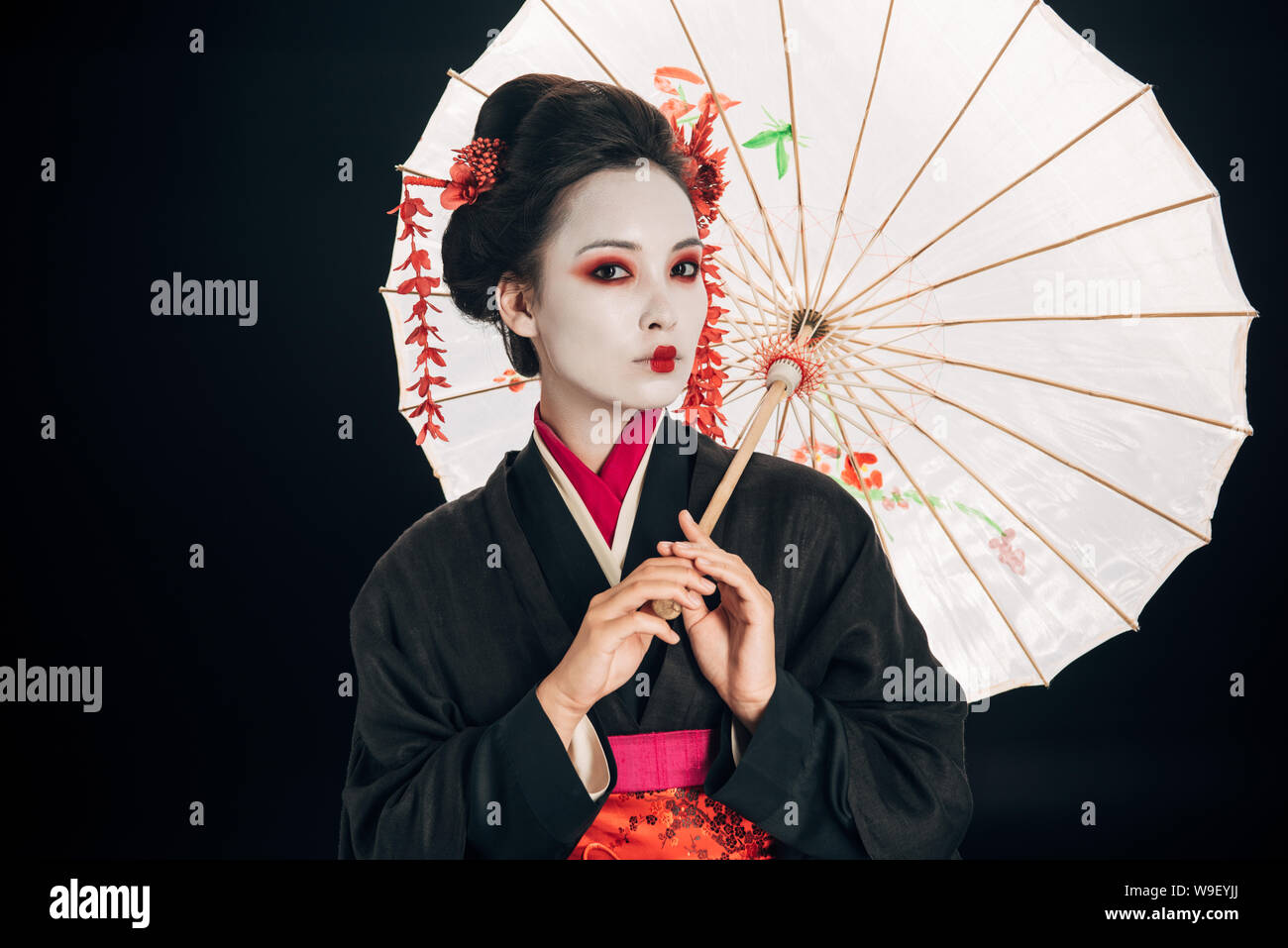 Hermosa geisha en el kimono negro con flores rojas en el cabello mantiene  aislado en paraguas negro asiático Fotografía de stock - Alamy
