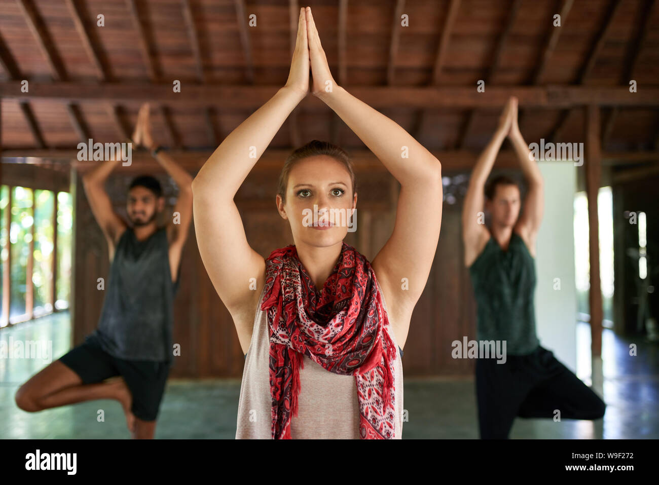 Hermosa hembra profesor dando clase de yoga a dos hombres de raza mixta en las esteras del yoga en templo tradicional en Bali Indonesia Foto de stock