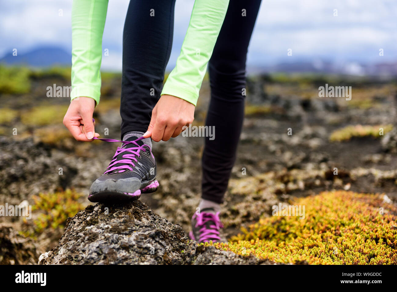 Trail Runner mujer preparándose para ejecutar sobre el barro de las  montañas rocosas en la carrera de otoño. Atleta atar los cordones de los  zapatos para correr. Primer plano de las manos