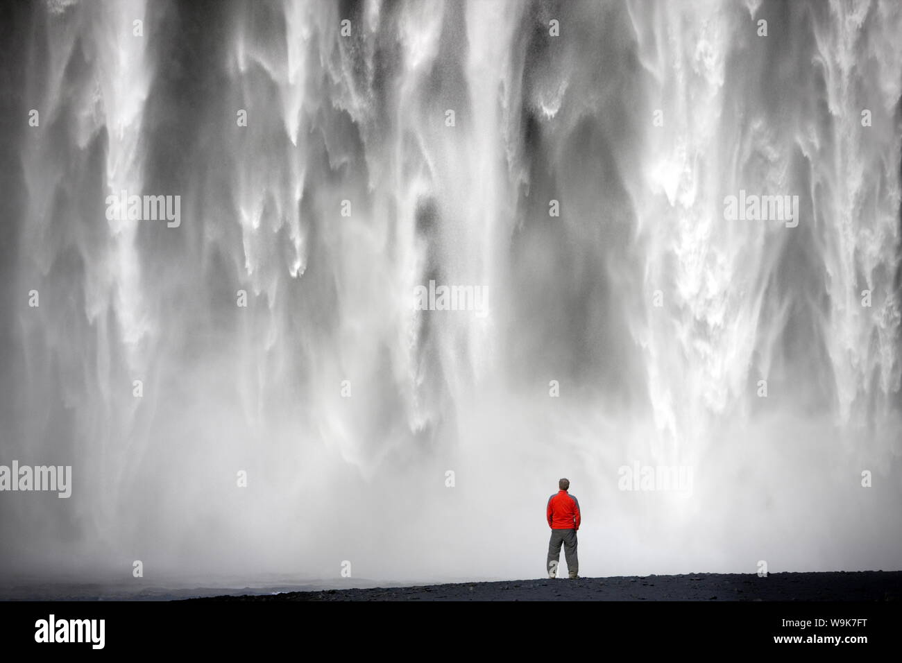 Hombre de chaqueta roja de pie delante de la Catarata Skogafoss 62m de altura, cerca de la aldea de Skogar, zona sur, Islandia, las regiones polares Foto de stock
