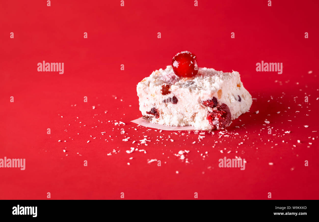 Rebanada de pastel de Navidad blanco con coco, frutos secos y cerezas, sobre un fondo rojo. Alimentos dulces tradicionales de Australia. Vacaciones de invierno postre Foto de stock