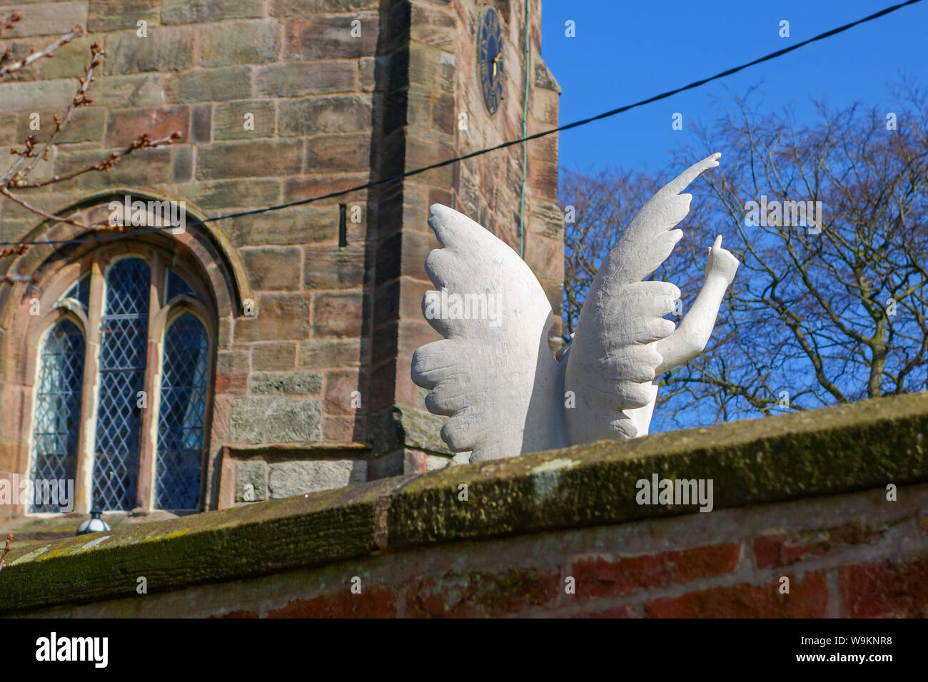 Un querubín alado o ángel memorial en una tumba en un patio de la Iglesia con las alas blancas y una mano y un dedo señalando hacia el cielo Foto de stock
