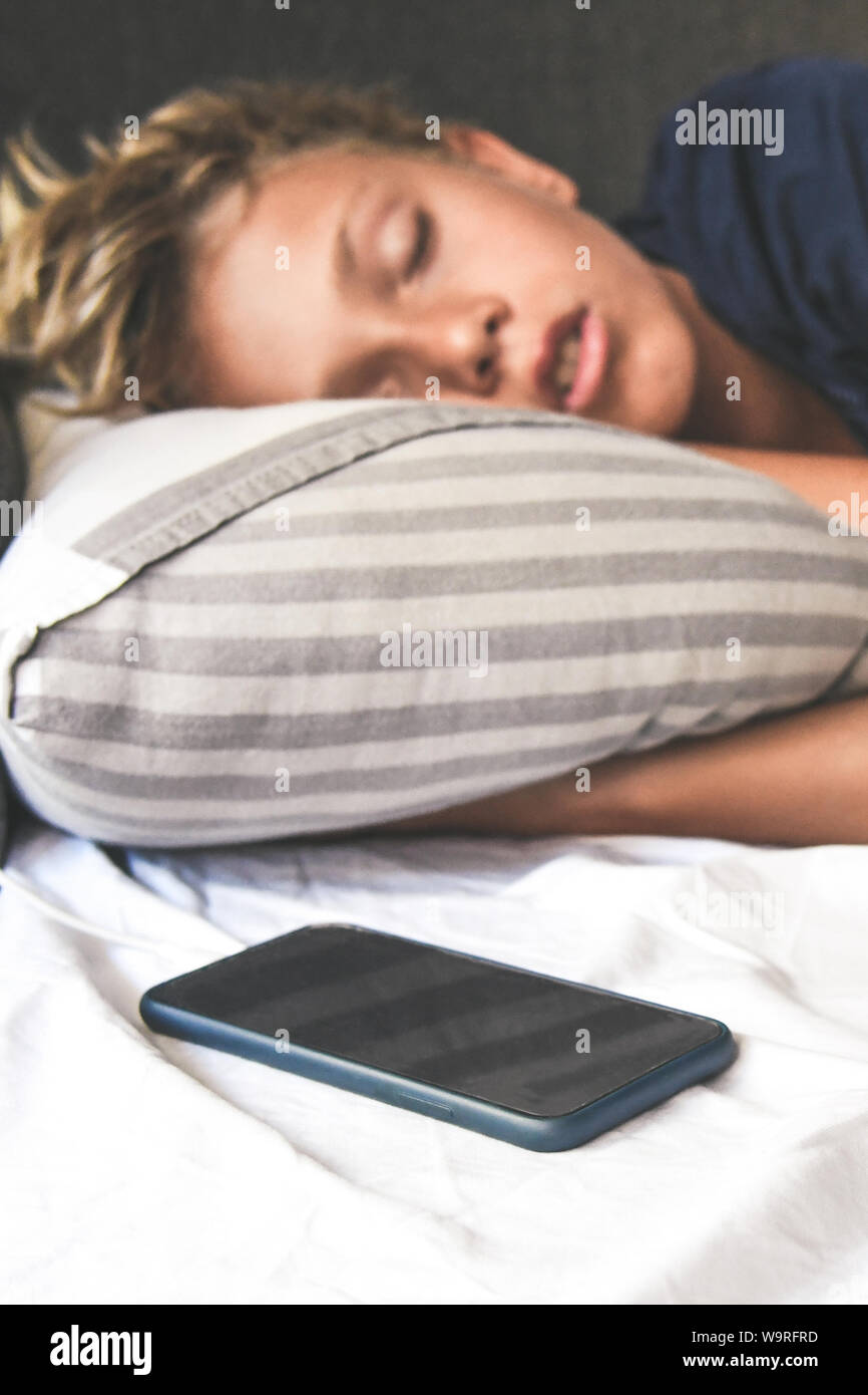 Joven dormir con las manos debajo de la almohada cerca del teléfono  celular. Hermoso niño duerme sola en la cama soñando con juegos en línea.  Agregar tecnología Fotografía de stock - Alamy