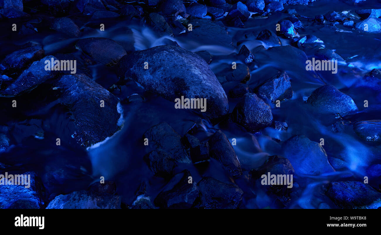 Piedras azules en stream con suave fluir agua por la noche. La larga exposición fotografía Foto de stock