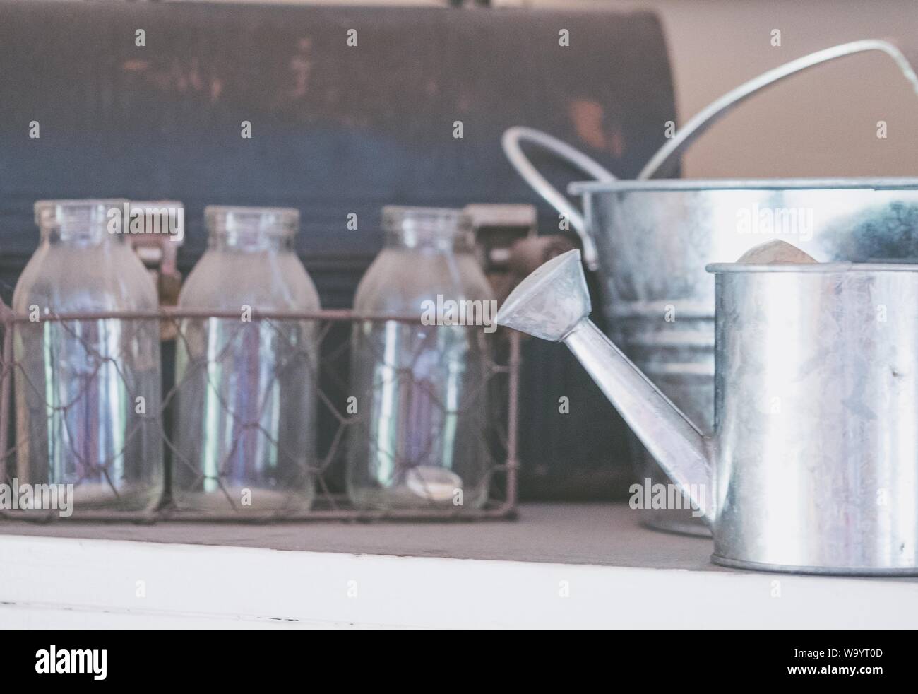 Primer plano de una lata de riego de metal, un cubo y botellas de vidrio en una cesta de metal Foto de stock
