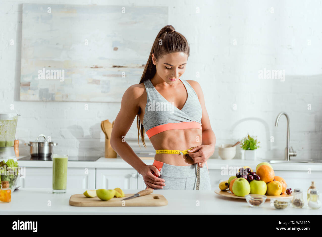 Mujer joven la medición de cintura cerca de frutas y bebidas Foto de stock