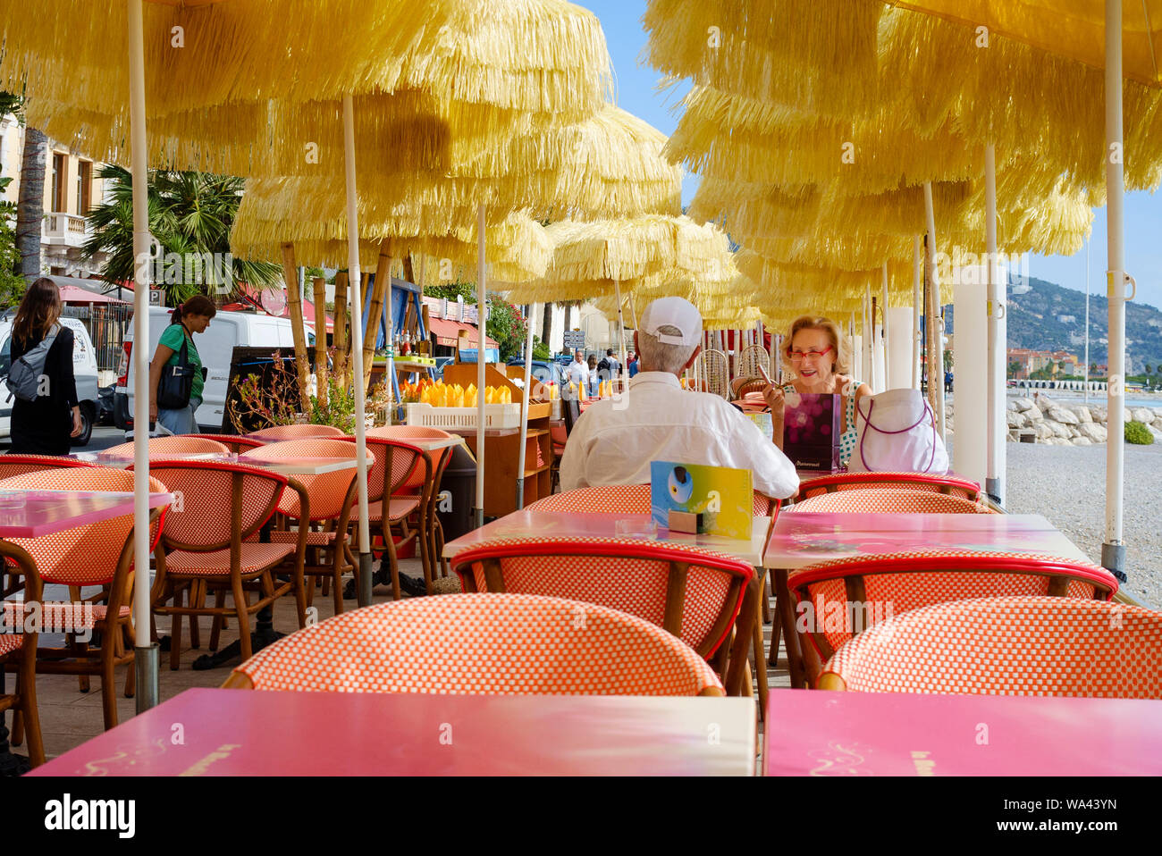 Pareja de ancianos, disfrutar de una comida al aire libre en una playa-side street café / restaurante en el casco antiguo de la ciudad de Menton en la Cote d'Azur de Francia del Sur Foto de stock