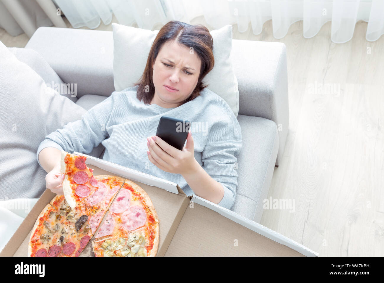 Triste mujer comer pizza y celebración teléfono acostado en un sofá en  casa, tono azul Fotografía de stock - Alamy