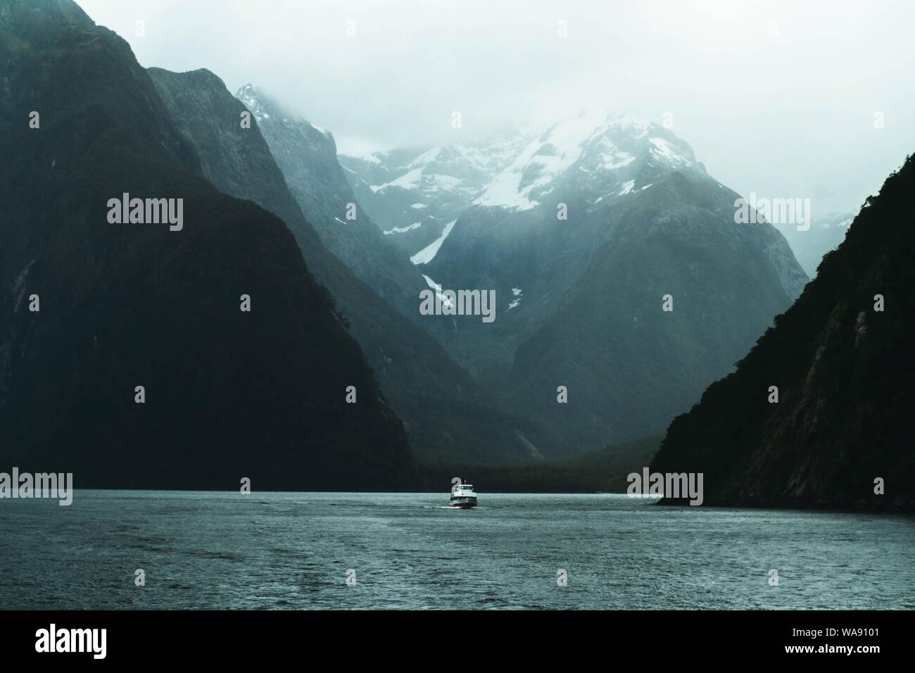 Un hermoso tiro de un lago con un barco de vela cuddy en el medio y en las montañas rocosas a ambos lados Foto de stock