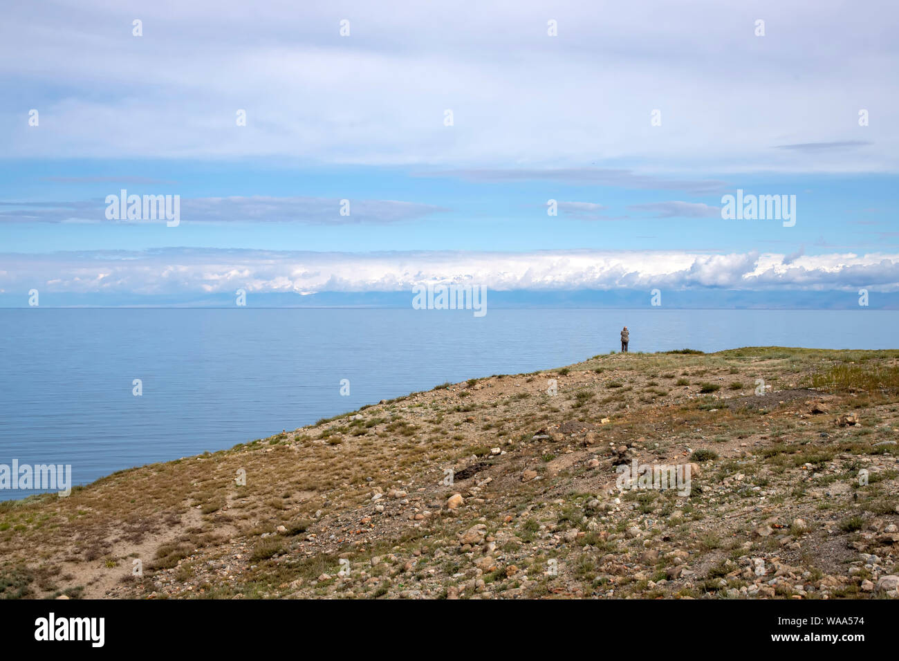 Un hombre de pie sobre una colina y mirando al lago Issyk-Kul y Ala-Too montañas. Kirguistán Foto de stock